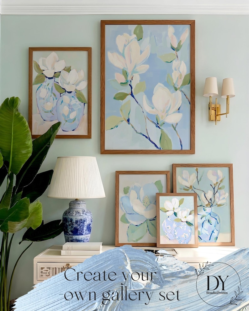 Puede incluir: Una pared de galer&iacute;a con impresiones art&iacute;sticas florales enmarcadas con flores de magnolia blancas y jarrones azules. Las obras de arte se exhiben en varios tama&ntilde;os con marcos de madera. Tambi&eacute;n se ve una l&aacute;mpara de cer&aacute;mica azul y blanca y un aplique dorado.