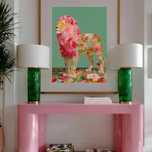 K&ouml;nnte beinhalten: Ein gerahmter Kunstdruck eines L&ouml;wen mit rosa und floraler M&auml;hne und K&ouml;rper, vor einem gr&uuml;nen Hintergrund. Das Kunstwerk wird &uuml;ber einem rosa Konsolentisch mit zwei gr&uuml;nen Lampen mit wei&szlig;en Schirmen ausgestellt. Der Raum hat ein modernes, dekoratives Thema.