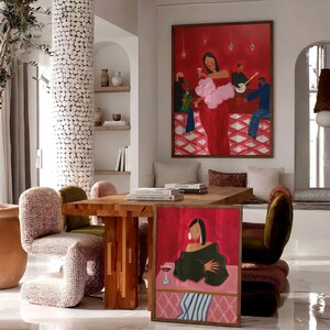 May include: An interior scene featuring a large framed painting of a woman in a red dress holding a glass of wine. A smaller painting with a similar theme is on the floor. The room includes a wooden table, chairs, and decorative elements, creating a stylish and artistic ambiance.