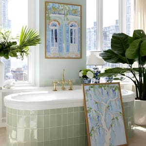 Puede incluir: Un ba&ntilde;o con una ba&ntilde;era ovalada blanca y grifos de lat&oacute;n, rodeado de azulejos verde claro. Dos cuadros enmarcados muestran escenas arquitect&oacute;nicas y bot&aacute;nicas. Tambi&eacute;n se ven una gran planta en maceta y una l&aacute;mpara blanca con una base estampada en azul y blanco.