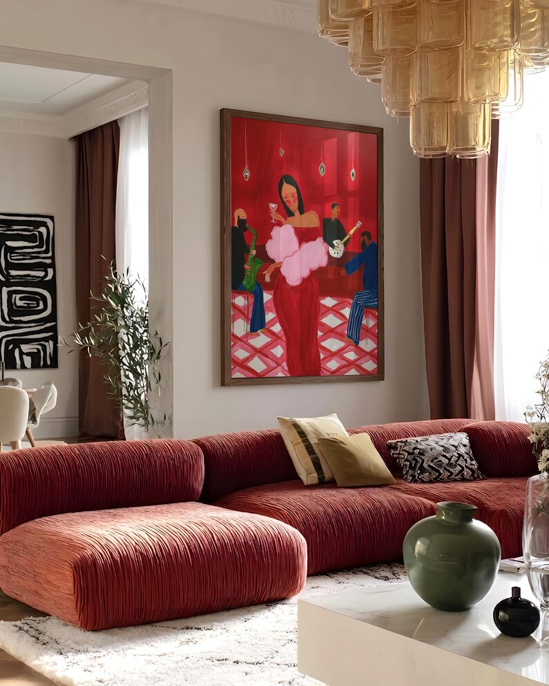 May include: A living room with a large red sofa and a framed painting. The painting depicts a woman in a red dress with a pink boa, with a band playing in the background. A green vase and decorative pillows are on the sofa.