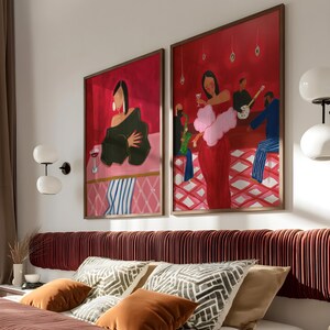May include: Two framed abstract art prints depicting figures in a bar setting, with a red and pink color scheme. The artwork is mounted above a bed with decorative pillows and a burgundy headboard. The room has a modern aesthetic.