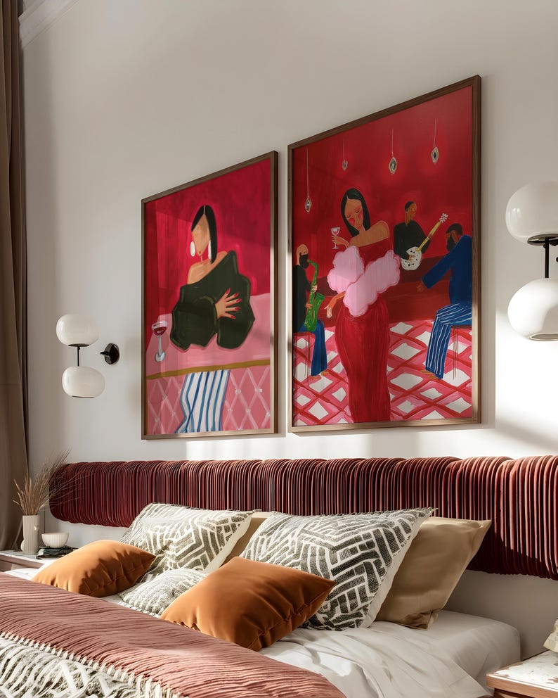May include: Two framed abstract art prints depicting figures in a bar setting, with a red and pink color scheme. The artwork is mounted above a bed with decorative pillows and a burgundy headboard. The room has a modern aesthetic.