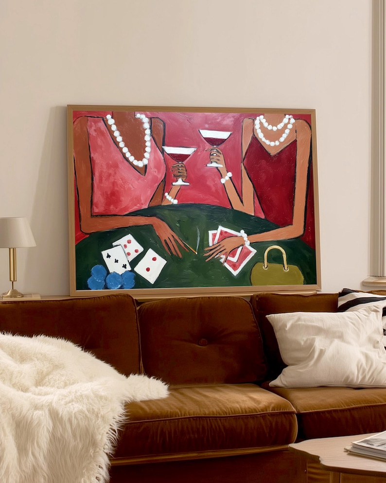 May include: An abstract painting depicts two figures at a poker table, holding wine glasses. The figures wear red and pink dresses and pearl necklaces. Playing cards, poker chips, and a purse are on the green table. The artwork is framed in a wooden frame.