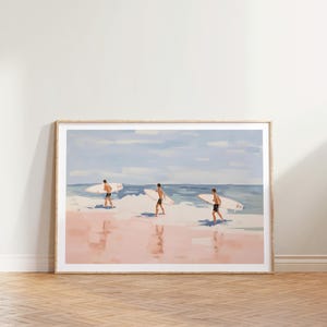 May include: A framed painting of three people walking on a beach with surfboards. The beach is pink and the water is blue. The sky is light blue with white clouds.