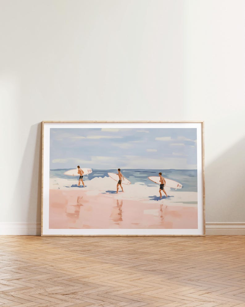May include: A framed painting of three people walking on a beach with surfboards. The beach is pink and the water is blue. The sky is light blue with white clouds.