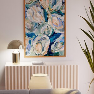 K&ouml;nnte beinhalten: Abstrakte Malerei von wei&szlig;en und blauen Blumen in einem Holzrahmen, die an einer wei&szlig;en Wand &uuml;ber einem hellbraunen Schrank mit einer Lampe darauf h&auml;ngt.