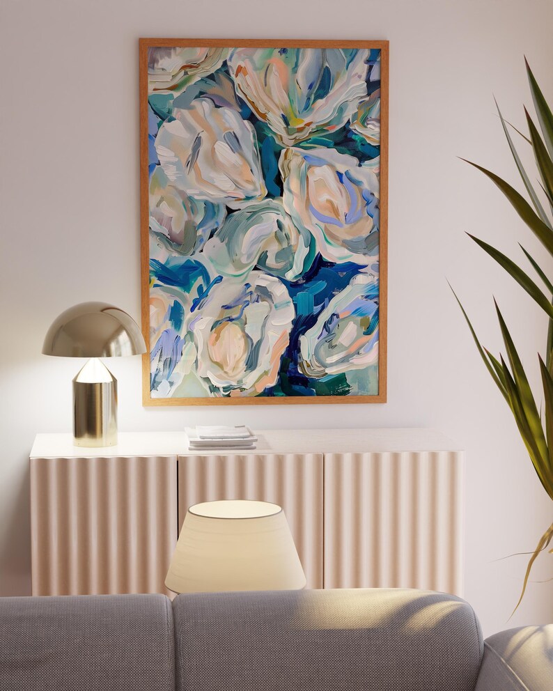 K&ouml;nnte beinhalten: Abstrakte Malerei von wei&szlig;en und blauen Blumen in einem Holzrahmen, die an einer wei&szlig;en Wand &uuml;ber einem hellbraunen Schrank mit einer Lampe darauf h&auml;ngt.