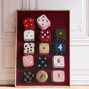 Op de afbeelding: Een ingelijst kunstwerk met twaalf dobbelstenen met verschillende ontwerpen. De dobbelstenen zijn geschilderd in kleuren als rood, wit, zwart, goud en roze, met verschillende punt- en symboolarrangementen. De achtergrond is dieprood.