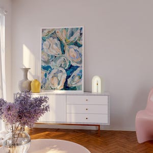 K&ouml;nnte beinhalten: Eine wei&szlig;e Kommode mit drei Schubladen und goldenen Kn&ouml;pfen steht in einem Wohnzimmer mit einem rosa Sessel, einer wei&szlig;en Lampe und einem Blumenbild an der Wand. Eine Vase mit lila Blumen steht auf einem rosa Couchtisch.