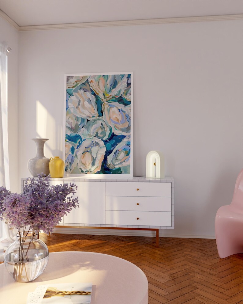 K&ouml;nnte beinhalten: Eine wei&szlig;e Kommode mit drei Schubladen und goldenen Kn&ouml;pfen steht in einem Wohnzimmer mit einem rosa Sessel, einer wei&szlig;en Lampe und einem Blumenbild an der Wand. Eine Vase mit lila Blumen steht auf einem rosa Couchtisch.
