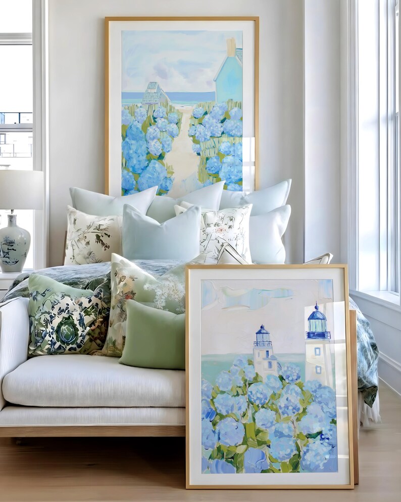 May include: A cozy living space featuring framed art with coastal scenes, including a lighthouse and a path to the beach. The room is decorated with light blue and green throw pillows, a white sofa, and a wooden floor.