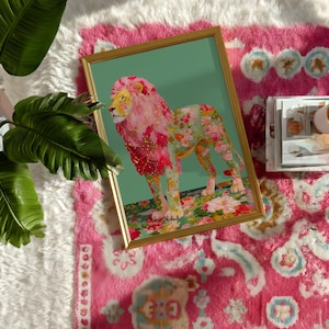 K&ouml;nnte beinhalten: Ein gerahmter Kunstdruck mit einem floralen L&ouml;wen auf gr&uuml;nem Hintergrund. Die M&auml;hne und der K&ouml;rper des L&ouml;wen sind mit bunten Blumen geschm&uuml;ckt. Der Druck liegt auf einem rosa Teppich mit wei&szlig;em, flauschigem Rand und einer gr&uuml;nen Pflanze.