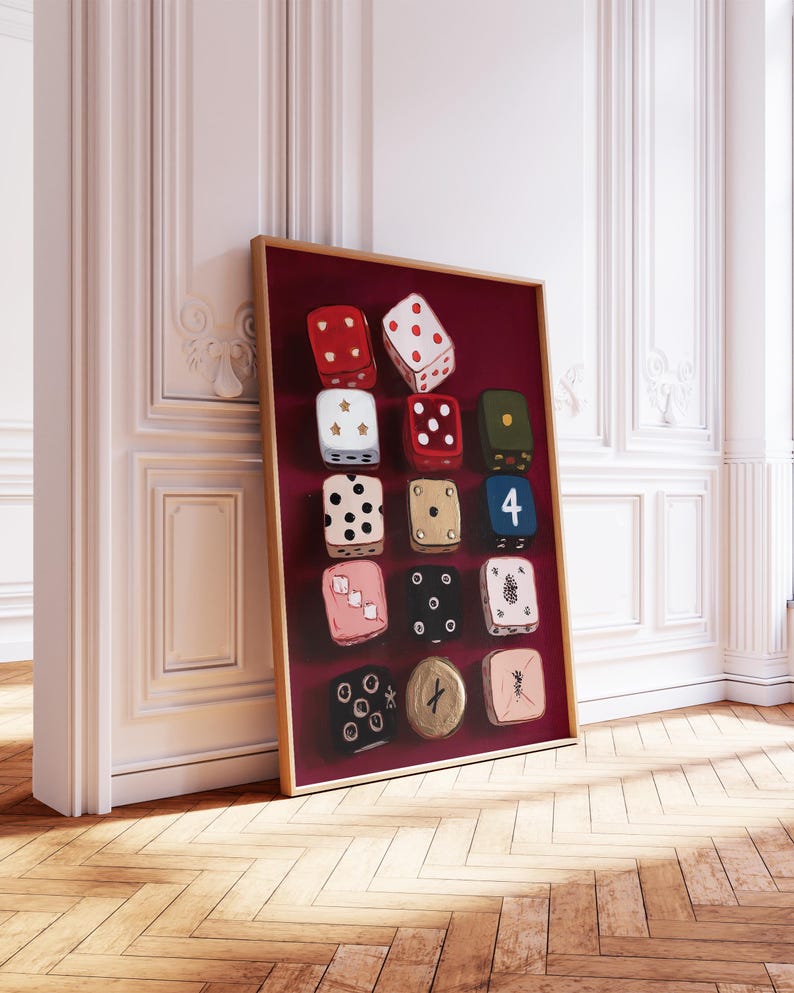 Op de afbeelding: Een ingelijst kunstwerk met een verzameling van twaalf dobbelstenen tegen een dieprode achtergrond. De dobbelstenen zijn geschilderd in verschillende kleuren, waaronder rood, zwart en roze, met witte ogen. Het kunstwerk wordt tentoongesteld in een kamer met witte muren en een houten vloer.