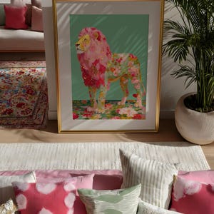K&ouml;nnte beinhalten: Ein gerahmter Kunstdruck mit einem L&ouml;wen mit rosa floraler M&auml;hne und K&ouml;rper. Das Kunstwerk ist vor einem gr&uuml;nen Hintergrund und in Gold gerahmt. Der Druck wird in einem Raum mit dekorativen Kissen und einem Teppich ausgestellt.