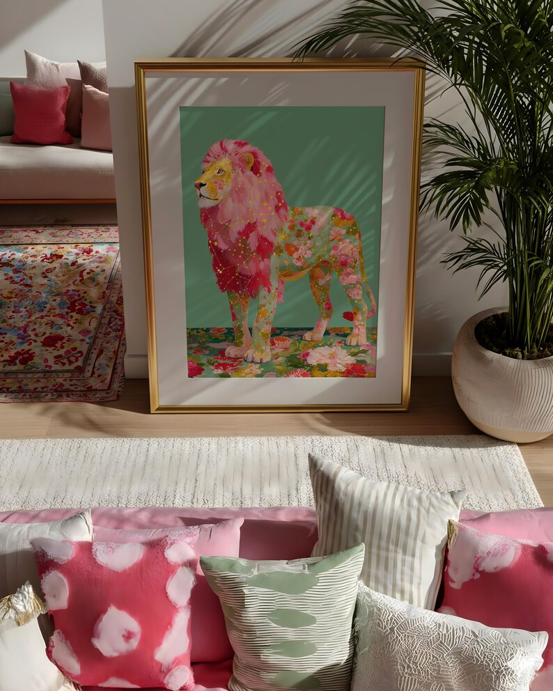 K&ouml;nnte beinhalten: Ein gerahmter Kunstdruck mit einem L&ouml;wen mit rosa floraler M&auml;hne und K&ouml;rper. Das Kunstwerk ist vor einem gr&uuml;nen Hintergrund und in Gold gerahmt. Der Druck wird in einem Raum mit dekorativen Kissen und einem Teppich ausgestellt.