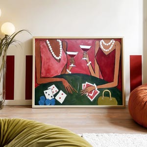 May include: An abstract painting depicts two figures in red dresses, each holding a martini glass. They are seated at a green table with playing cards, poker chips, and a purse. The artwork is framed in a light wood.