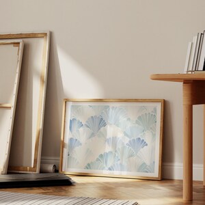 May include: A framed print with a blue and white watercolor pattern of overlapping fan shapes. The print is hanging on a white wall in a room with wooden floors and a wooden table.