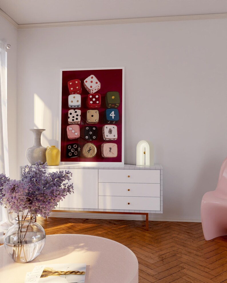Op de afbeelding: Een ingelijste kunstdruk met twaalf dobbelstenen in verschillende kleuren, waaronder rood, wit, groen en roze, tegen een dieprode achtergrond. De dobbelstenen tonen verschillende punt- en cijfercombinaties. Het kunstwerk wordt in een moderne woonkamer gepresenteerd.