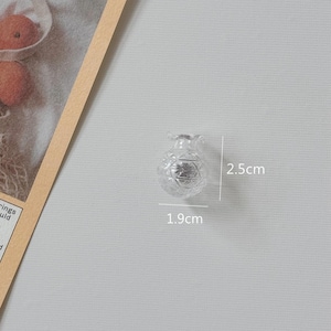 K&ouml;nnte beinhalten: Eine kleine, klare Glasvase mit einem detaillierten Schliffmuster. Die Vase ist 1,9 cm breit und 2,5 cm hoch. Die Vase befindet sich auf einem hellgrauen Hintergrund.