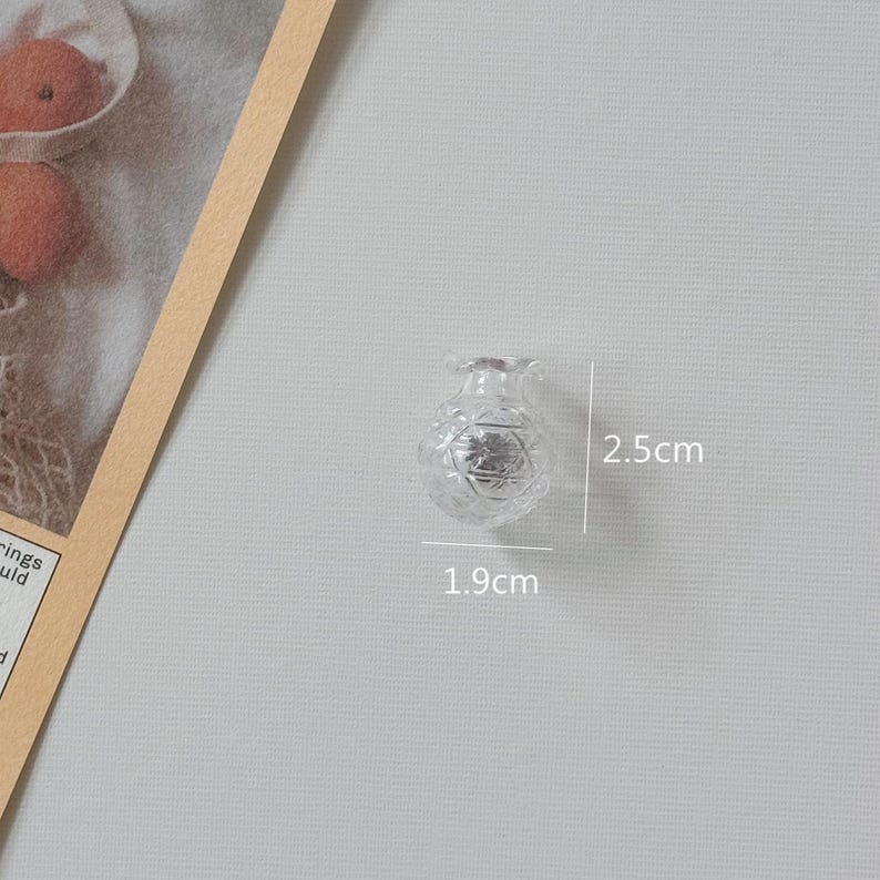 K&ouml;nnte beinhalten: Eine kleine, klare Glasvase mit einem detaillierten Schliffmuster. Die Vase ist 1,9 cm breit und 2,5 cm hoch. Die Vase befindet sich auf einem hellgrauen Hintergrund.