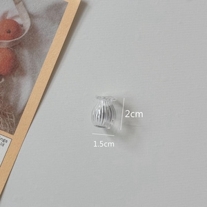 K&ouml;nnte beinhalten: Eine kleine, transparente Glasvase mit geriffeltem Design. Die Vase ist etwa 2 cm hoch und 1,5 cm breit. Sie hat einen ger&uuml;schten oberen Rand und eignet sich f&uuml;r kleine Blumenarrangements oder dekorative Zwecke.