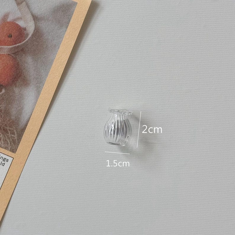 K&ouml;nnte beinhalten: Eine kleine, transparente Glasvase mit geriffeltem Design. Die Vase ist etwa 2 cm hoch und 1,5 cm breit. Sie hat einen ger&uuml;schten oberen Rand und eignet sich f&uuml;r kleine Blumenarrangements oder dekorative Zwecke.