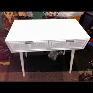 May include: White mid-century style desk with two drawers. The drawers have a woven cane design and brass-coloured handles. The desk has four tapered legs. The desk is approximately 120 cm long.