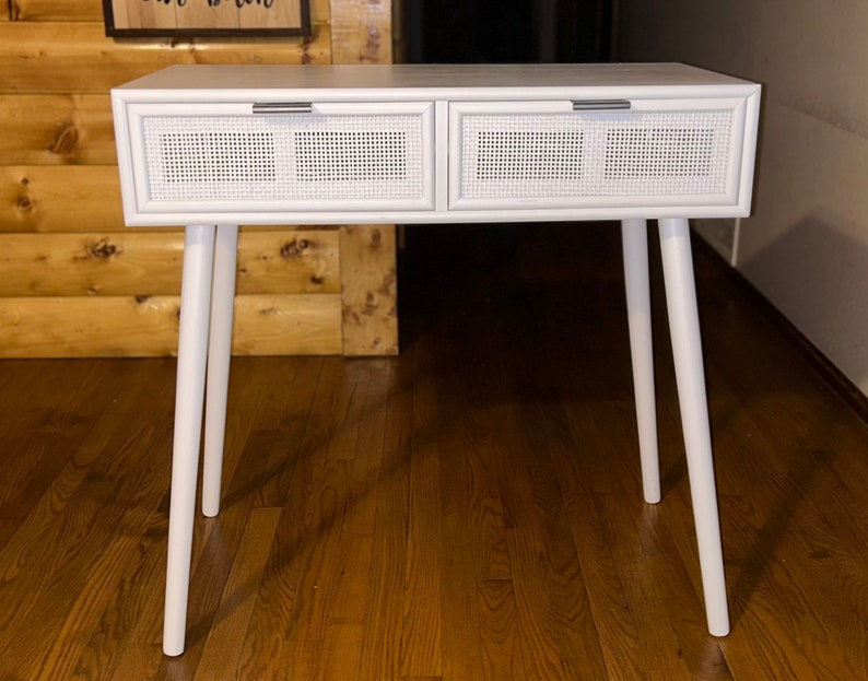 May include: White console table with two drawers featuring woven cane fronts and silver handles. The table has four angled, tapered legs. A stylish piece for any room.