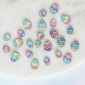 May include: A collection of pastel colored Easter eggs with a chevron pattern. The eggs are arranged on a white marble surface.
