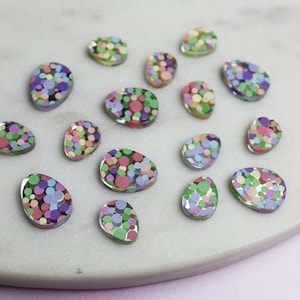 May include: Assortment of colorful confetti-filled resin egg-shaped ornaments. The ornaments are translucent and feature a variety of colors, including pink, purple, green, and blue.