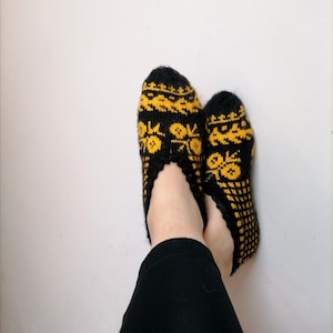Peut inclure: Une paire de chaussettes de pantoufles en tricot noir et jaune avec un motif géométrique.