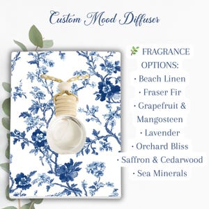 May include: A custom mood diffuser with a round glass bottle and a wooden top, hanging in front of a white background with a blue floral pattern. The text lists fragrance options: Beach Linen, Fraser Fir, Grapefruit & Mangosteen, Lavender, Orchard Bliss, Saffron & Cedarwood, and Sea Minerals.