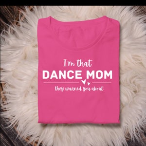Puede incluir: Camiseta rosa con el texto "I'm that DANCE MOM they warned you about" en blanco.