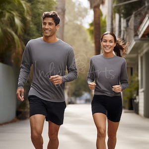 Puede incluir: Dos personas con camisas grises de manga larga están trotando por una calle. El hombre lleva pantalones cortos negros y la mujer lleva pantalones cortos negros.