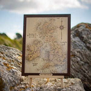 May include: A wooden map of the British Isles, framed in dark brown, displayed on a small wooden easel. The map features detailed geographical outlines and text, including "North Atlantic Ocean" and "Celtic Sea". The words "British Isles" are at the bottom.