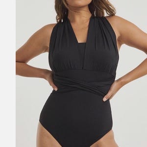 Puede incluir: Un bañador de una pieza en color negro liso con un escote en V profundo y tejido fruncido en el busto. El cuerpo incluye tirantes anchos y un detalle de cintura estilo envolvente que se cruza sobre la sección media del torso.