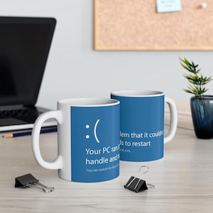 May include: Two white ceramic mugs with blue interiors. The mugs feature a blue and white design with a sad face emoticon and the text "Your PC ran into a problem that it couldn't handle and needs to restart."