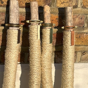 May include: Four wooden posts wrapped in natural rope with brass rings and leather straps. The posts are mounted on a brick wall.