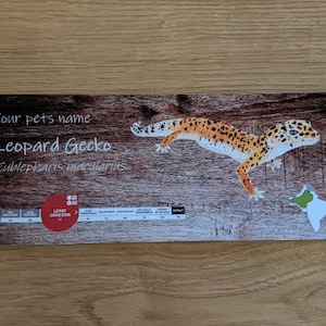 May include: A brown and white wooden sign with a leopard gecko illustration. The sign says "Your pet's name Leopard Gecko Eublepharis macularius" and has a red circle with the text "Least Concern" in it.