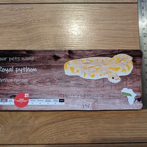 May include: A wooden card featuring a drawing of a royal python snake, with the text "Royal python" and "Python regius" printed on it. The card also includes a map of Africa with a green area highlighting the snake's natural habitat. The card is labelled "Near Threatened".