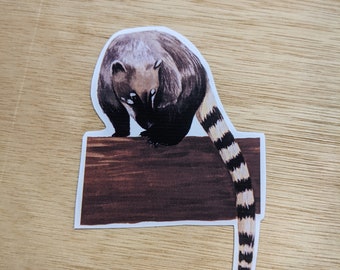May include: A sticker of a brown and white animal with a long, striped tail. The animal is standing on a brown log and is looking down.