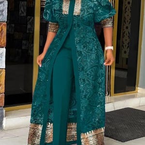 May include: A teal green ensemble featuring a long, open-front jacket with intricate floral lace detailing and gold trim. The jacket has short, puffed sleeves and is paired with matching teal pants. The outfit is a formal, elegant style.