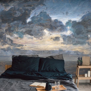 May include: A bedroom featuring a mural of a stormy sky in blue, grey, and gold hues. The bed has dark blue cushions and a grey blanket. A wooden step stool holds candles and a plant.