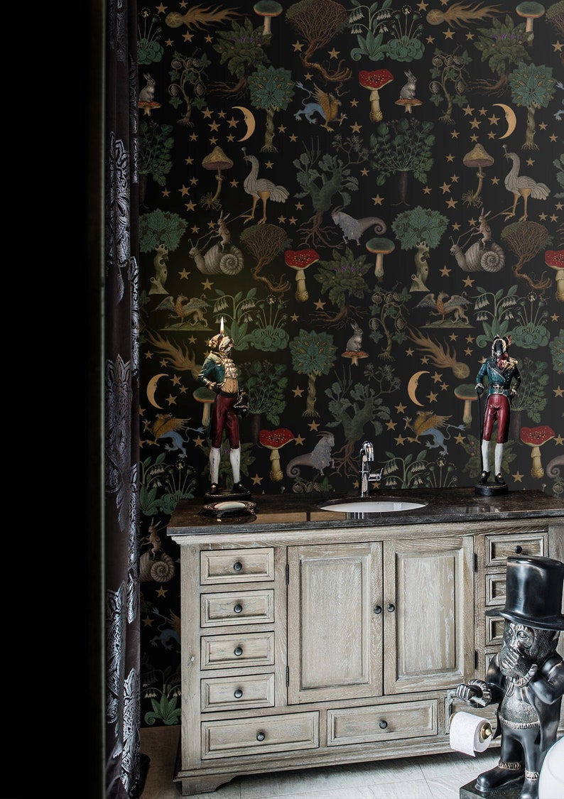 May include: A bathroom vanity with a black countertop and a white wooden cabinet with six drawers and two doors. The vanity is decorated with two figurines and a black and white wallpaper with a whimsical forest scene featuring mushrooms, stars, and animals.