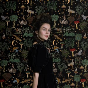 May include: A woman in a black velvet dress stands in front of a dark background with a repeating pattern of stars, mushrooms, and other whimsical creatures. The pattern is in shades of green, gold, and red.