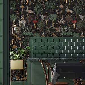 May include: A dark green kitchen with a black and gold wallpaper featuring a whimsical forest scene with mushrooms, stars, and mythical creatures. The wallpaper is on the wall behind a green tiled backsplash and a dark green cabinet. There are two wooden chairs with black cushions and a black tablecloth on the table.
