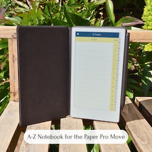 Puede incluir: Cuaderno de cuero marrón abierto con una pantalla digital que muestra una lista. La pantalla muestra las palabras "A Notes" y "Details". El cuaderno está sobre un banco de madera con follaje verde en el fondo. El texto "A-Z Notebook for the Paper Pro Move" está en la parte inferior.