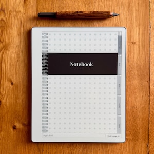 May include: A digital tablet displaying a notebook interface with a dot grid pattern, a black horizontal band labeled Notebook, and side navigation tabs. A wooden stylus with a dark tip is positioned horizontally above the tablet screen.