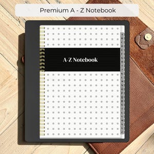 Peut inclure: Un carnet A-Z noir avec une reliure à spirale, avec un motif à pois blancs sur les pages. Le carnet a une bande noire avec le texte "A-Z Notebook". Le carnet est à l'intérieur d'un étui en cuir marron. Le texte "Premium A - Z Notebook" est en haut.